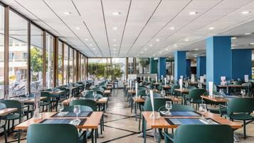 A spacious indoor dining area with multiple tables and chairs, large windows, and a modern ceiling design.
