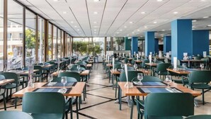 Un restaurante espacioso con techos altos, ventanas amplias y sillas verdes. Las mesas están ordenadas con menús y copas.