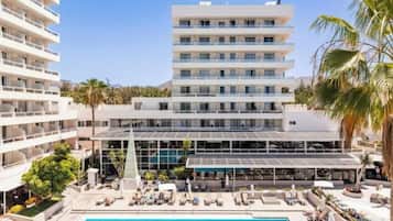 A hotel with a swimming pool, multiple balconies, and a covered outdoor seating area.