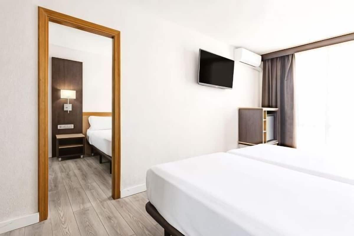 Ein Hotelzimmer mit einem Bett, einem an der Wand befestigten Fernseher, einem Schreibtisch mit Lampe und einem Kleiderschrank.