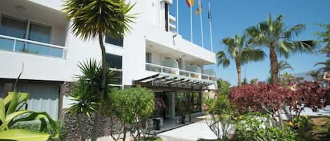 A hotel with a covered entrance, palm trees, and flags.