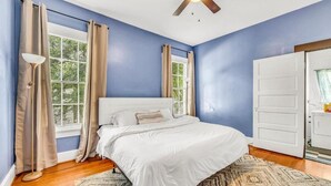 Une chambre à coucher avec un lit, des rideaux, un ventilateur de plafond et une fenêtre donnant sur un paysage verdoyant.