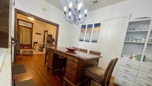 Un coin repas avec une table en bois, des chaises et un lustre. Il y a également un coin cuisine avec des placards et un réfrigérateur.