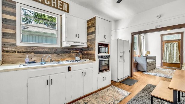 Une cuisine moderne avec des armoires blanches, un mur d’accent en bois et une vue sur l’extérieur.
