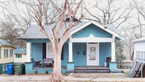 Une maison de plain-pied avec un porche, un arbre devant et une boîte aux lettres sur la porte d’entrée.