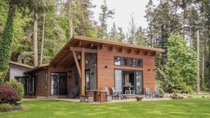 Une cabane moderne en bois, dotée d’une grande terrasse et entourée d’une végétation luxuriante.