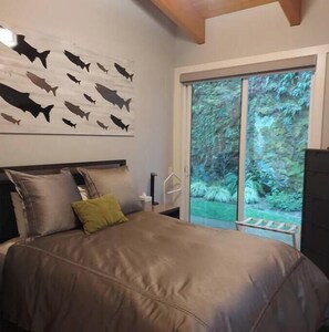 A bedroom with a bed, pillows, a wall art of fish, and a sliding glass door to a garden. - Secluded, peaceful, ocean front home. Close to all amenities/outdoor activities. (Sooke)