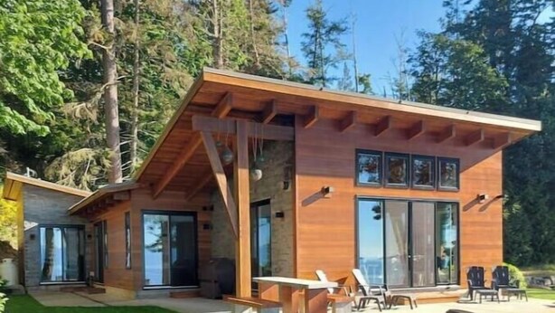 Une maison moderne avec une façade en bois, de grandes portes-fenêtres coulissantes et un patio aménagé avec du mobilier d’extérieur.
