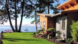 Une maison moderne dotée d’une pelouse bien entretenue, d’une terrasse en bois et d’une vue sur l’océan.