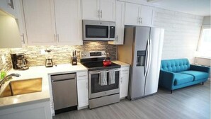 A modern kitchen with white cabinets, a microwave, a stove, and a refrigerator. There's a blue sofa in the living area.