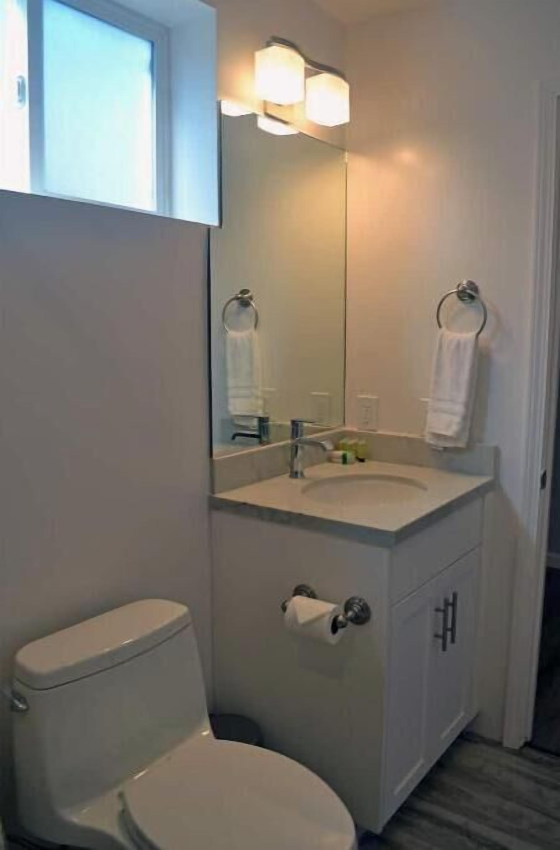 A bathroom with a toilet, sink, mirror, and towel rack.
