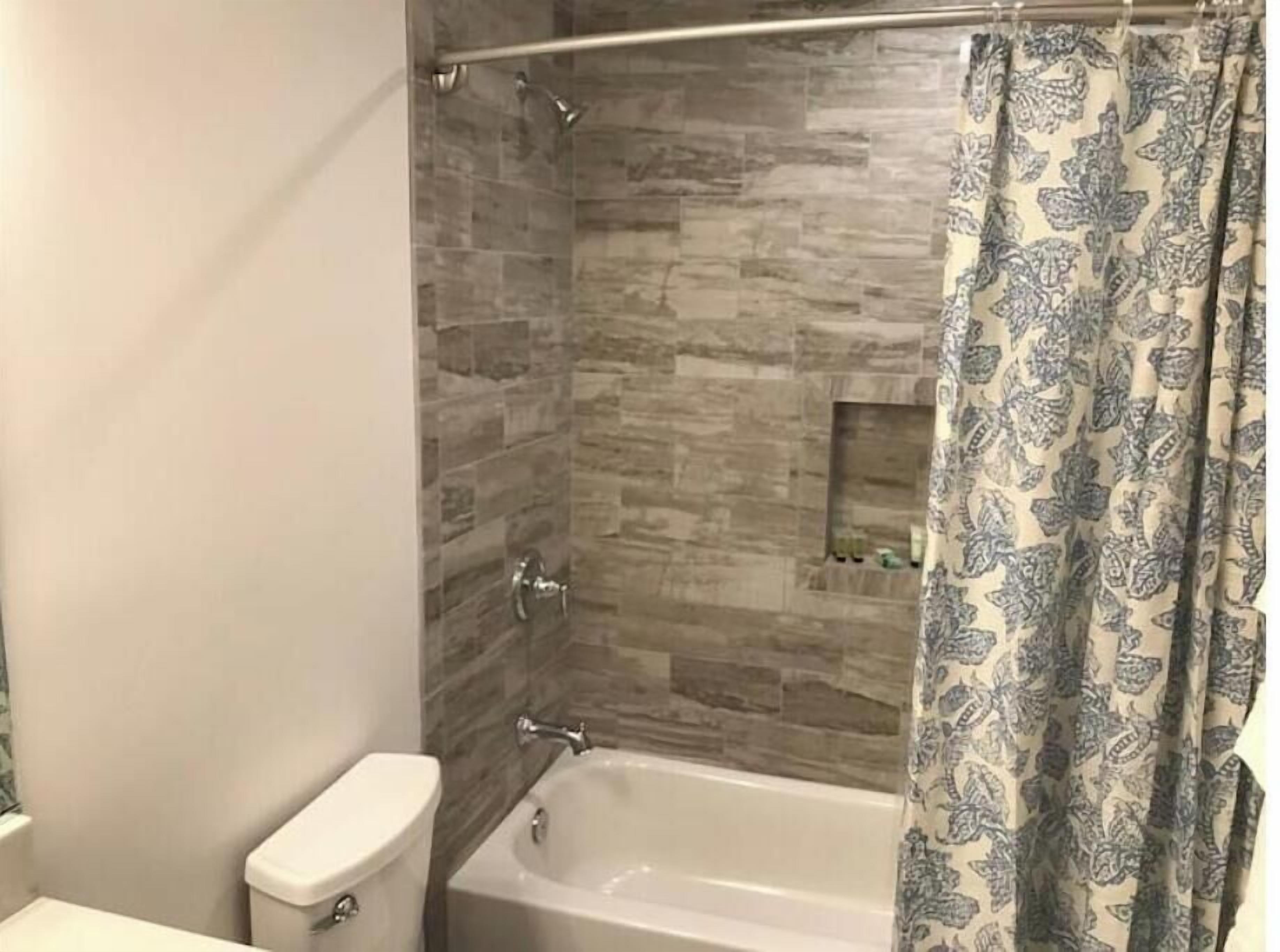 Et badeværelse med bruser, toilet og badekar.