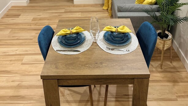 A dining table set with blue plates and yellow napkins, a glass, and a wooden floor. - The Prairie Nest (Saskatoon)