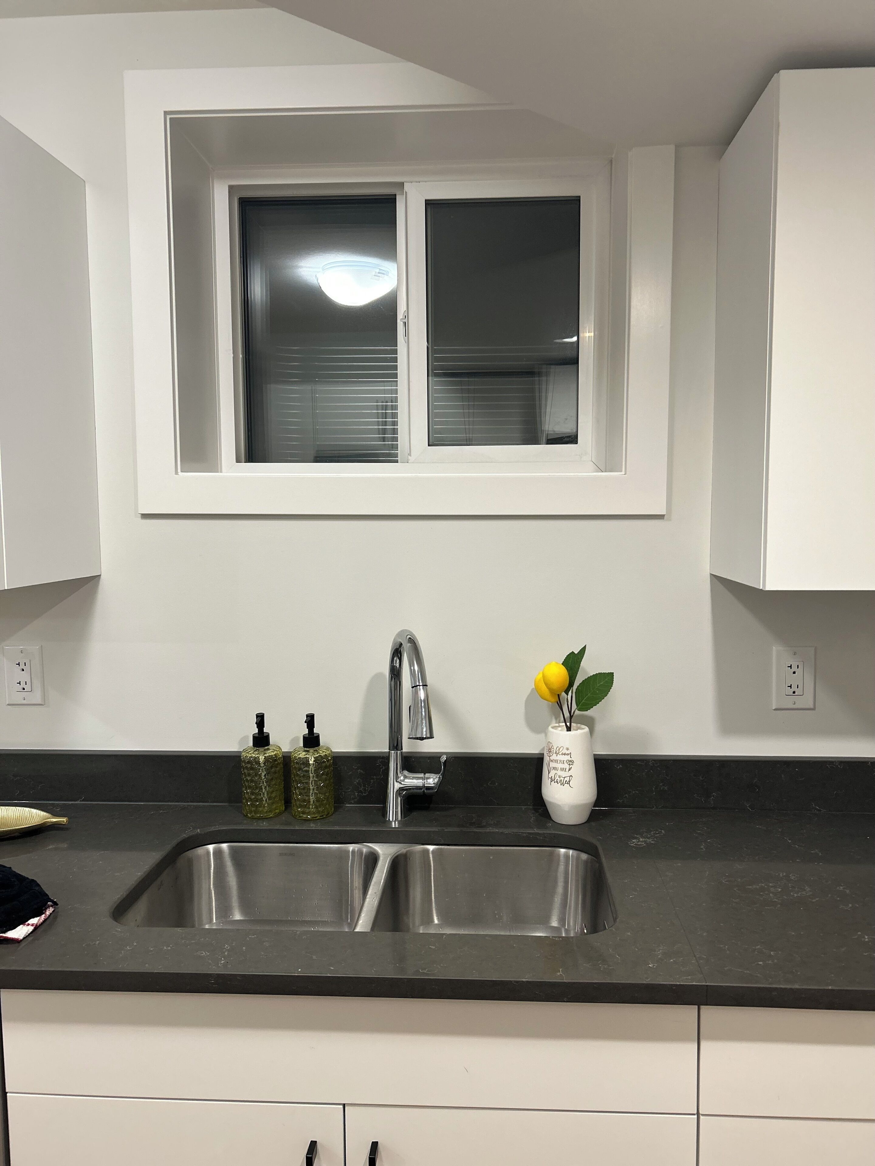A kitchen with a double sink, a window above the sink, and a vase with flowers on the counter.