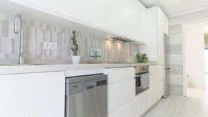 Una cocina moderna con armarios blancos, lavavajillas integrado, horno y grifo de acero inoxidable.