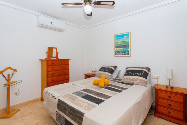 Un dormitorio con cama, cómoda de madera, mesitas de noche y ventilador de techo.