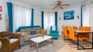 A living room with a sofa, a coffee table, a dining table with chairs, a ceiling fan, and curtains. - CH Villa Oceania La Marquesa Golf (Ciudad Quesada)