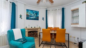 A living room with a teal armchair, a dining table with orange chairs, a fireplace, and a painting on the wall. - CH Villa Oceania La Marquesa Golf (Ciudad Quesada)