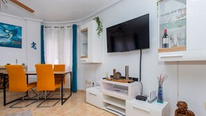 A modern living room with a dining area, a flat-screen TV mounted on the wall, and a glass cabinet with wine bottles. - CH Villa Oceania La Marquesa Golf (Ciudad Quesada)