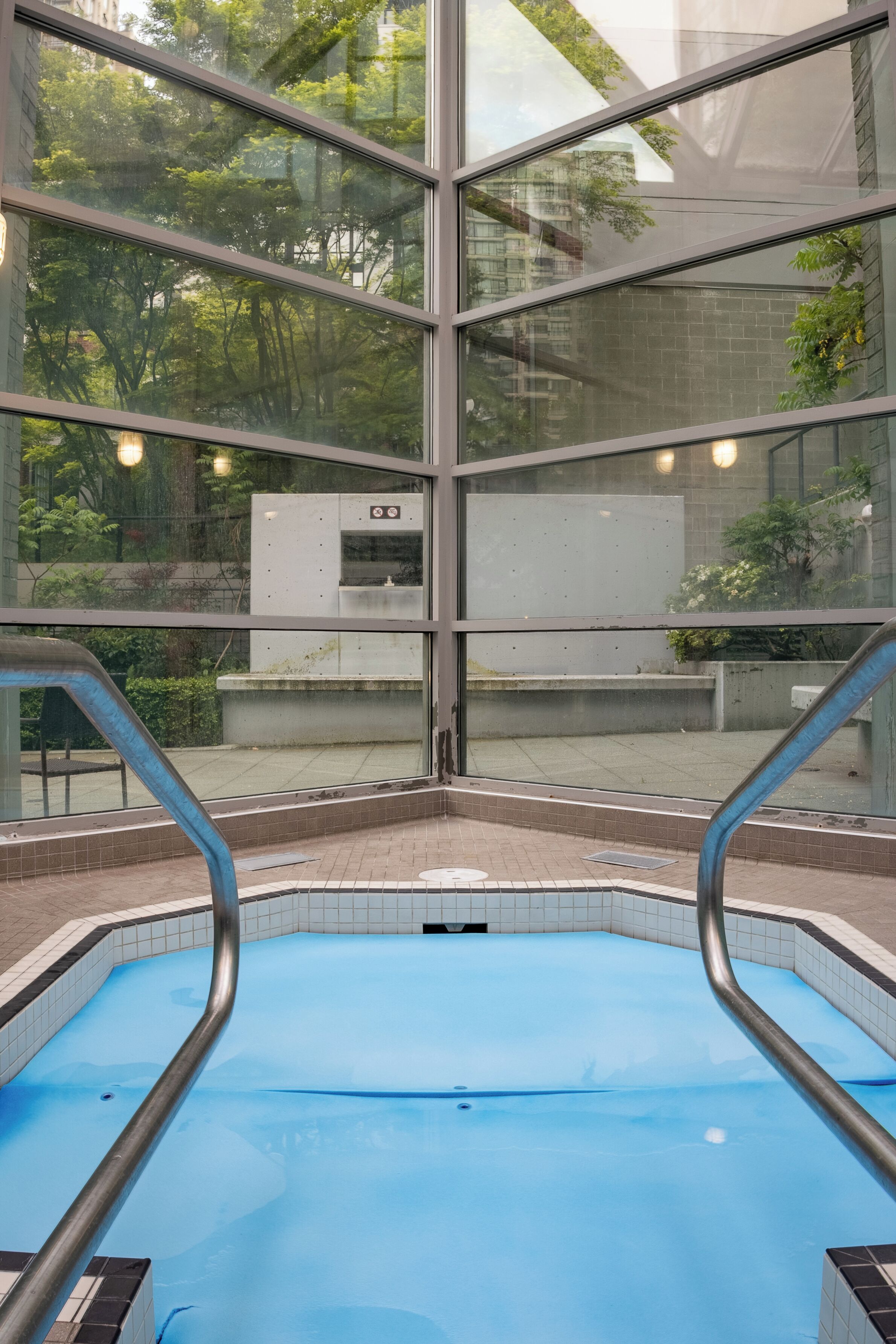A swimming pool with clear glass walls, a tiled floor, and metal handrails.