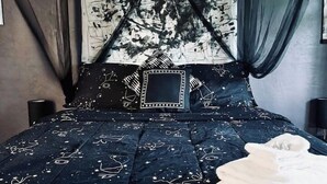 Una cama con colcha azul oscuro adornada con motivos de estrellas y luna, almohada blanca y dosel negro.