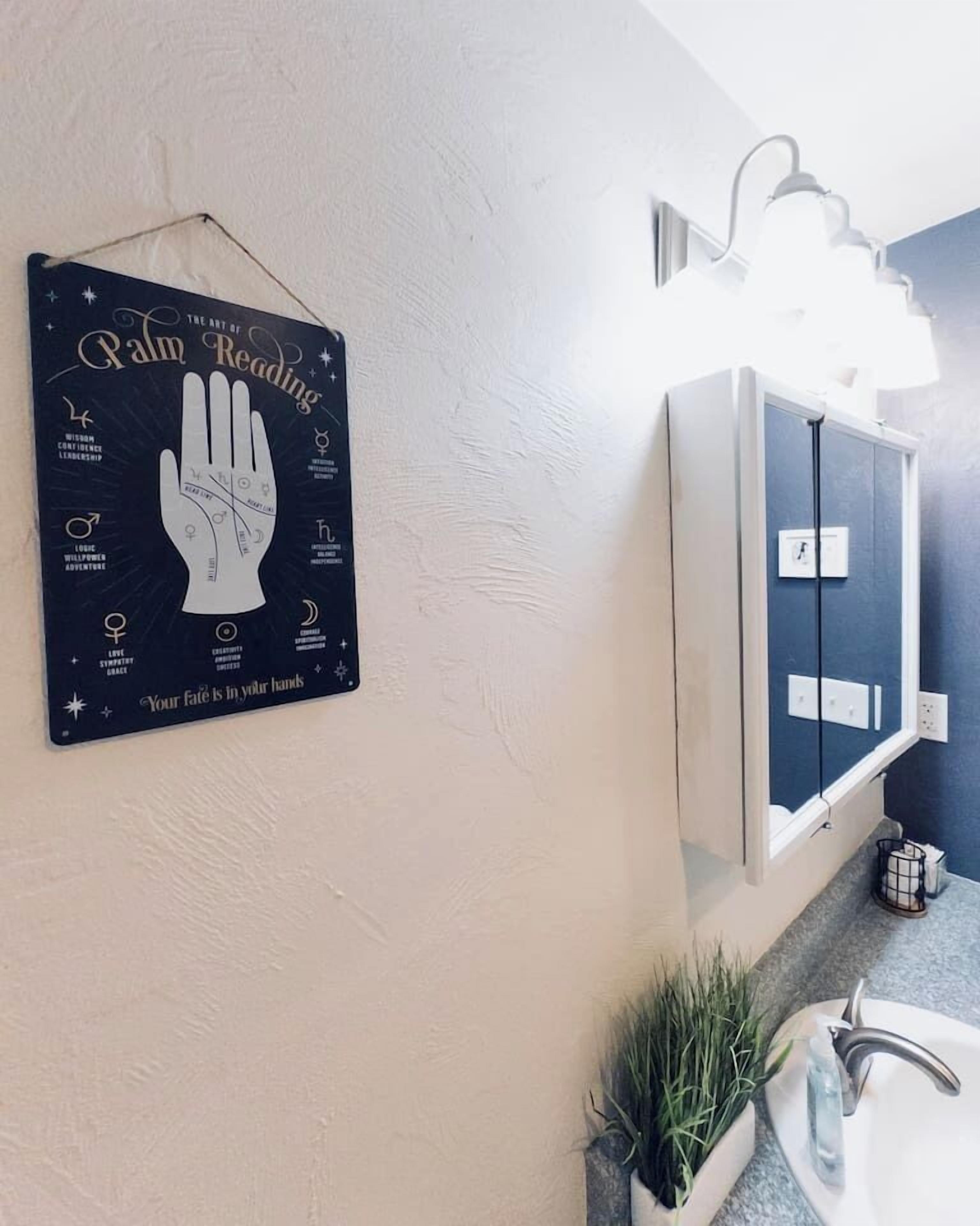 Een badkamer met een spiegel bevestigd aan de muur, een handbeschilderd bord met symbolen, en een potplant.