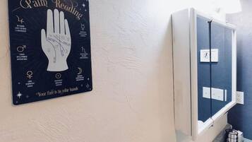 Een badkamer met een spiegel bevestigd aan de muur, een handbeschilderd bord met symbolen, en een potplant.