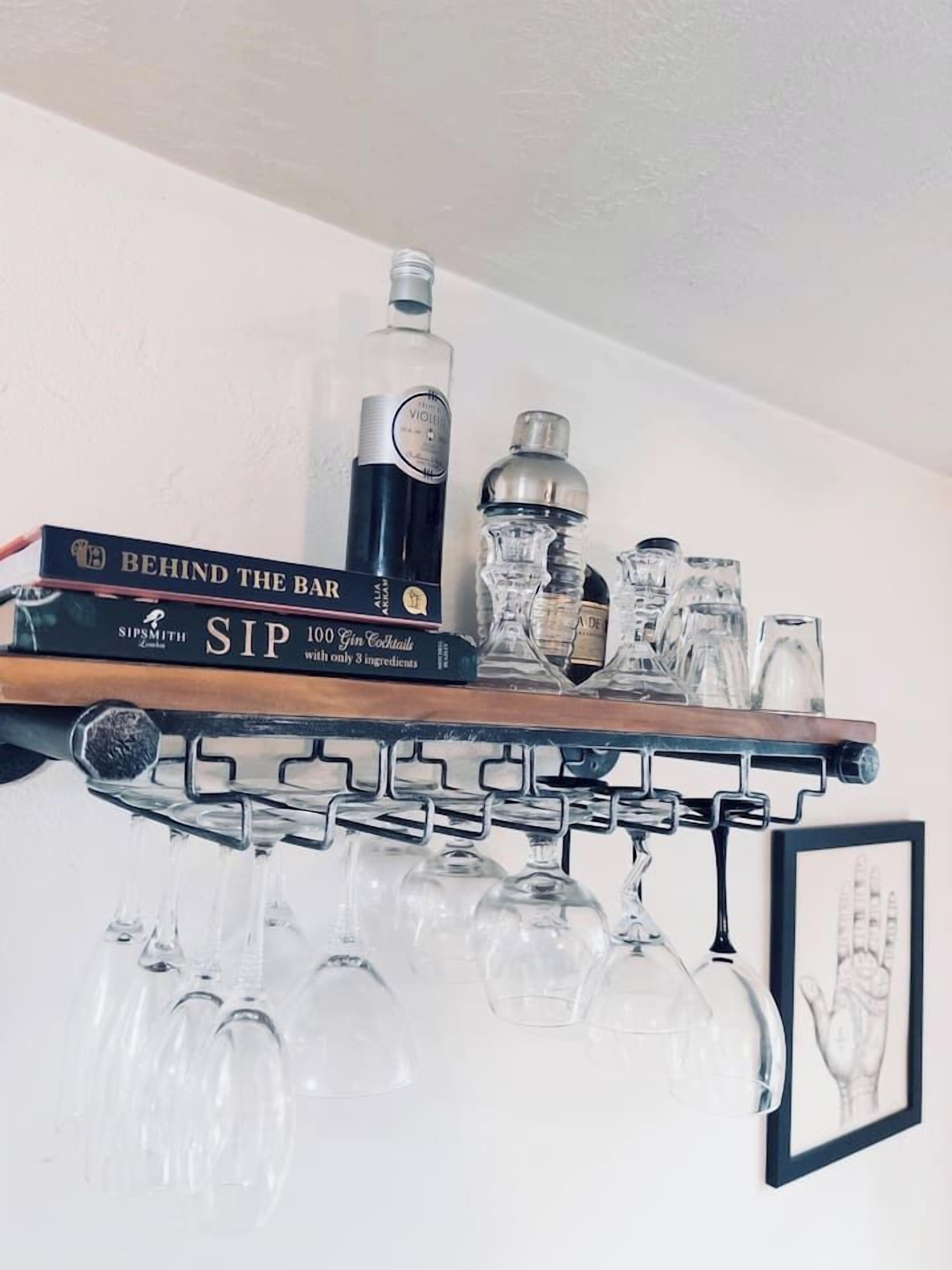 A bar shelf with a book titled 'Behind the Bar', a bottle of liquor, and several glasses.