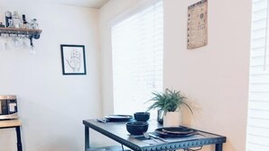 Una cocina compacta con una pequeña mesa de comedor, dos taburetes, una planta en maceta y un microondas.