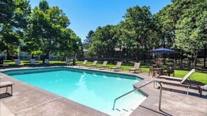 Una piscina rectangular con un deck de baldosas, rodeada de sillas de descanso y un pabellón.