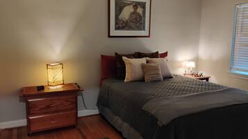 Een slaapkamer met een bed, een nachtkastje met een lamp, een houten dressoir en een schilderij aan de muur.