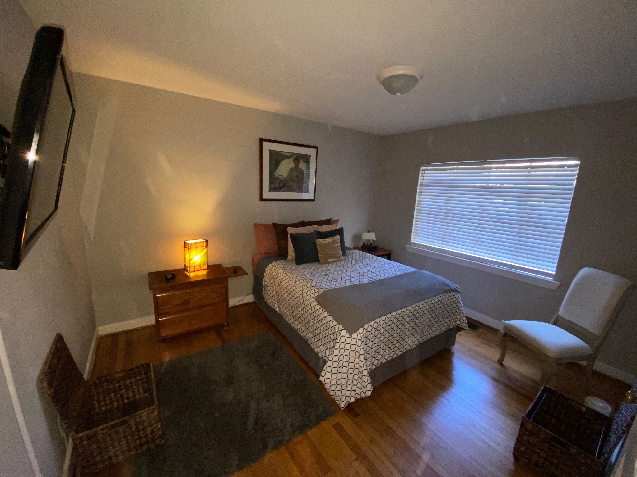 A bedroom with a bed, bedside tables, a chair, a window with blinds, a picture on the wall, and a floor lamp.