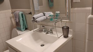A bathroom with a white sink, a towel rack with towels, a glass soap dispenser, and a mirror above the sink.