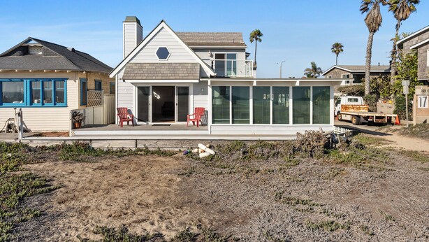 A modern house with a large glass front, a covered porch with red chairs, and a truck parked nearby.