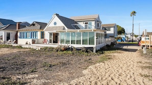 A beachfront house with a large glass front, a covered porch, and a sandy beach in the foreground.
