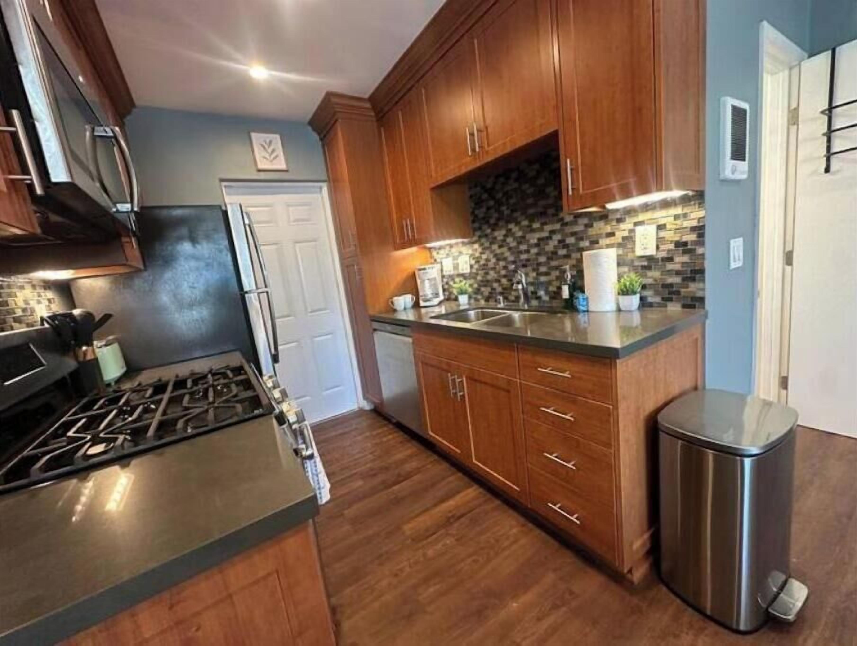A kitchen with wooden cabinets, a stainless steel stove, a sink, and a trash can.