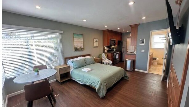 Habitación de hotel compacta con cama, mesita de noche, silla y una pequeña mesa de comedor.