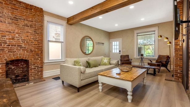 A spacious living room with a brick fireplace, a beige sofa, a wooden coffee table, and leather chairs. - Franklin Park Gem - Historic meets Modern w/ Space for the Whole Crew - 4BR, 2BA (Columbus)
