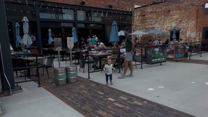 An outdoor seating area with tables and umbrellas, a brick building with 'Columbus' signage, and a child walking. - Franklin Park Gem - Historic meets Modern w/ Space for the Whole Crew - 4BR, 2BA (Columbus)