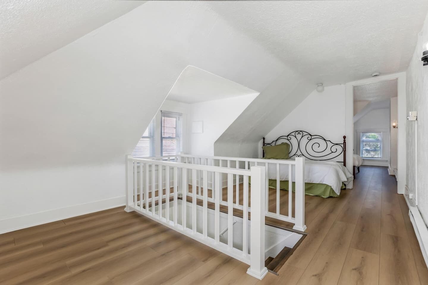 A room with a sloped ceiling, a white crib, a bed with green bedding, and a wooden floor.