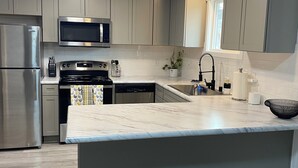 Une cuisine moderne avec des meubles gris, des appareils en acier inoxydable et un plan de travail en marbre.