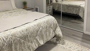 Une chambre à coucher comprenant un lit, une table de chevet, un miroir et une porte coulissante donnant sur une autre pièce.