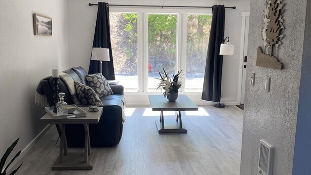 Un salon moderne avec un canapé, une table basse et une vue sur un jardin grâce à de grandes fenêtres.