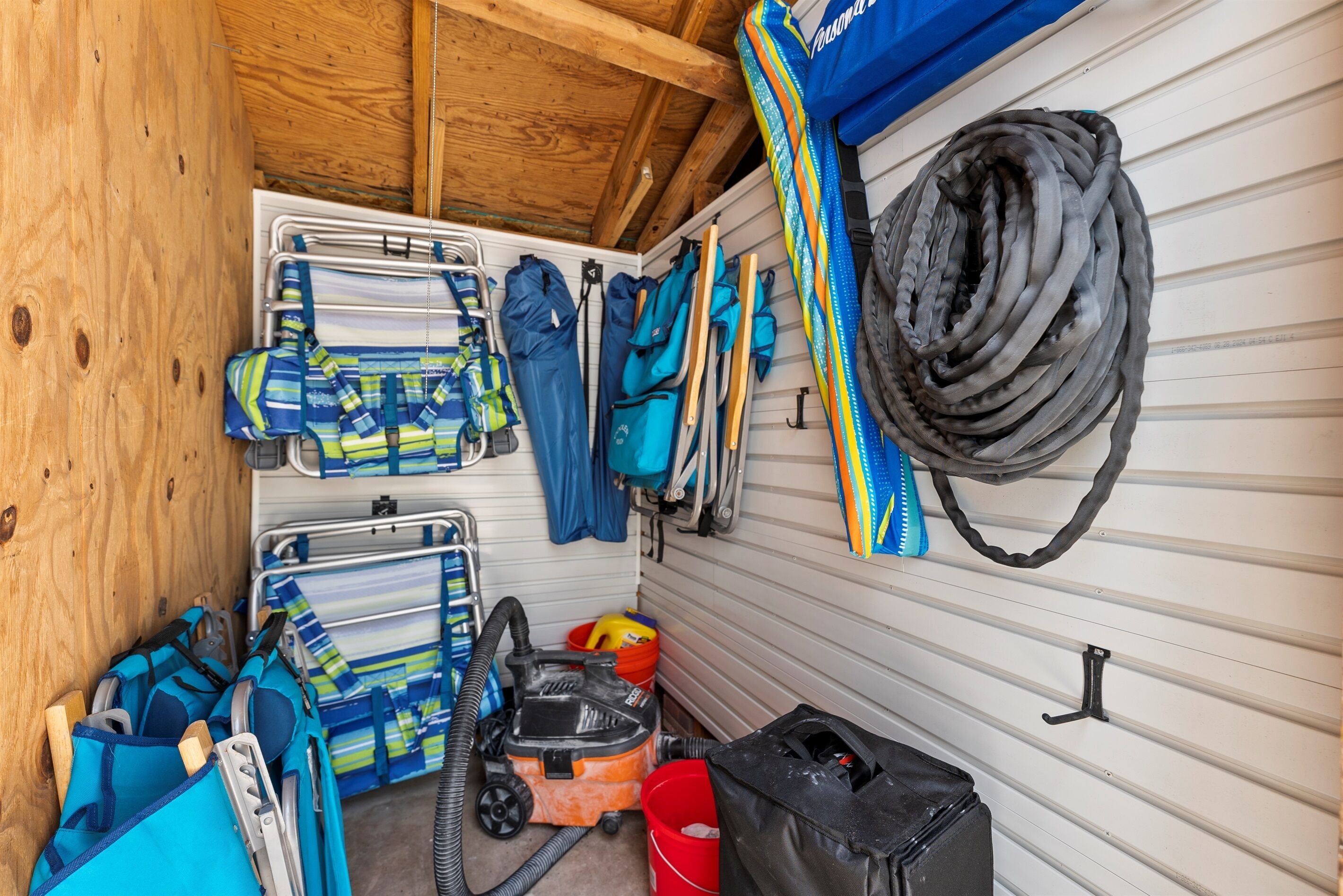 A storage area with various items including a vacuum cleaner, a red bucket, and multiple blue and green bags.