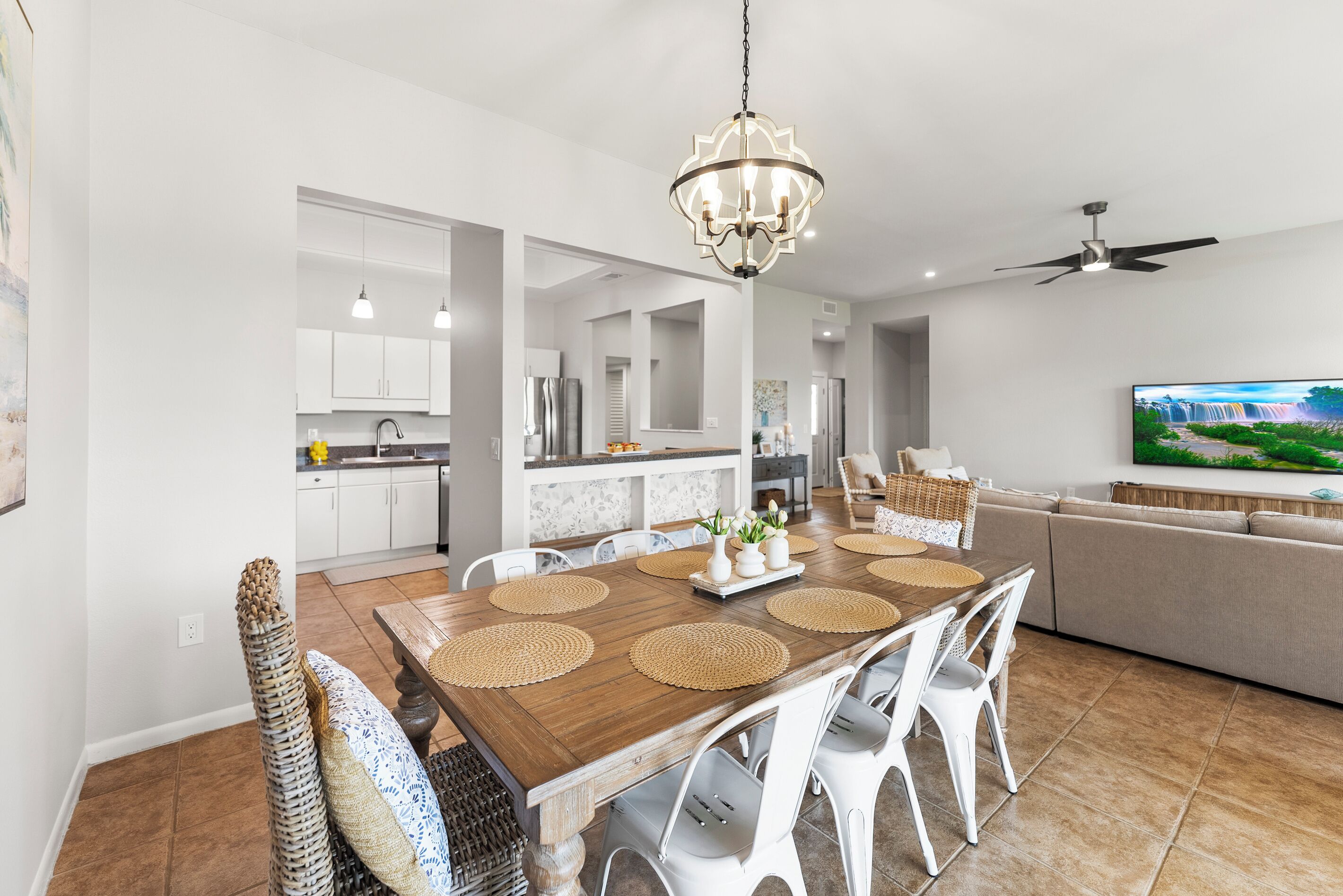 A modern dining area with a wooden table, white chairs, and a chandelier.