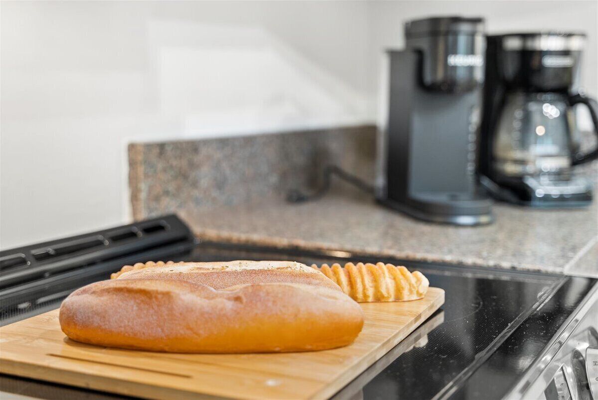 A loaf of bread on a wooden cutting board in a kitchen with a coffee maker in the background.
