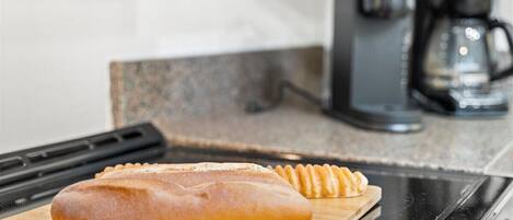 A loaf of bread on a wooden cutting board in a kitchen with a coffee maker in the background.