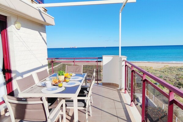 Un balcon avec une table préparée pour le petit-déjeuner, donnant sur une plage et la mer.