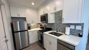 A modern kitchen with stainless steel appliances, white cabinetry, and a tiled backsplash.