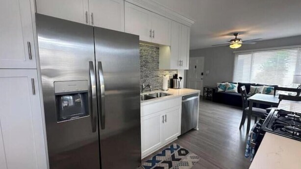 A modern kitchen with stainless steel appliances, white cabinetry, and a dining area with a patterned rug.
